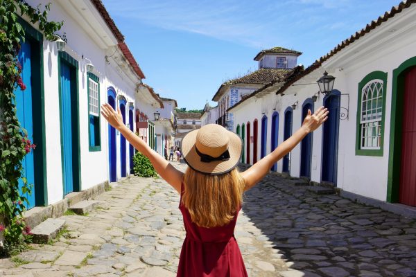 Joyful girl in Paraty, Brazil. Beautiful young woman with raised arms walking in colorful historic town of Paraty, UNESCO World Heritage Site, Brazil.